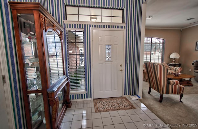 foyer entrance with visible vents, ornamental molding, wallpapered walls, carpet, and tile patterned flooring