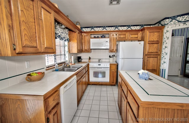 kitchen with visible vents, tile counters, brown cabinetry, white appliances, and a sink