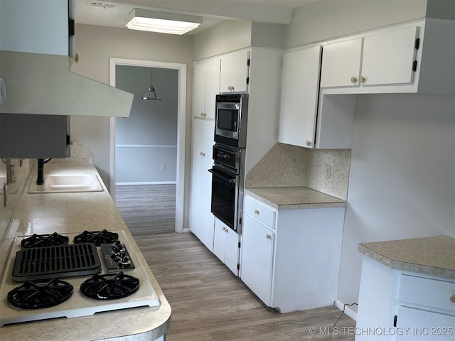 kitchen with white gas cooktop, light wood finished floors, a sink, oven, and stainless steel microwave