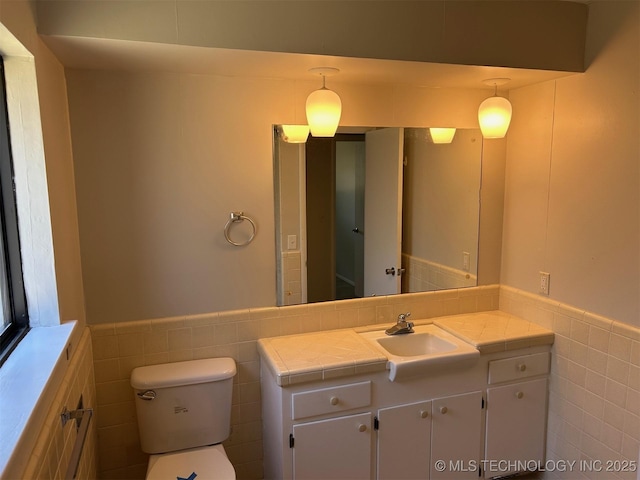 bathroom with vanity, toilet, tile walls, and wainscoting