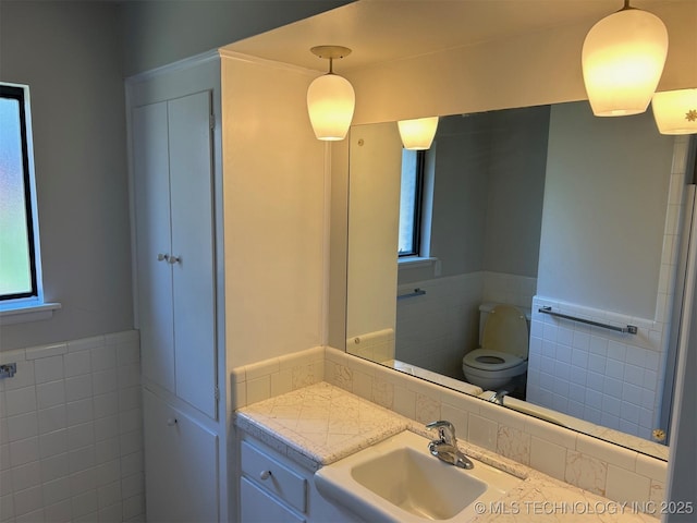 bathroom featuring a sink, a wainscoted wall, plenty of natural light, and tile walls