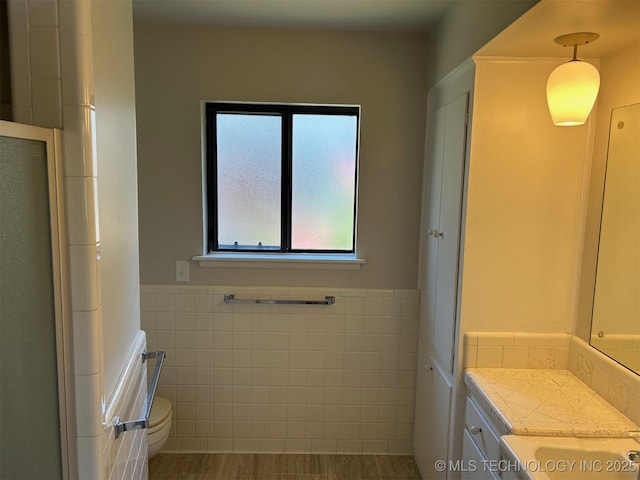 full bath with toilet, vanity, wainscoting, an enclosed shower, and tile walls