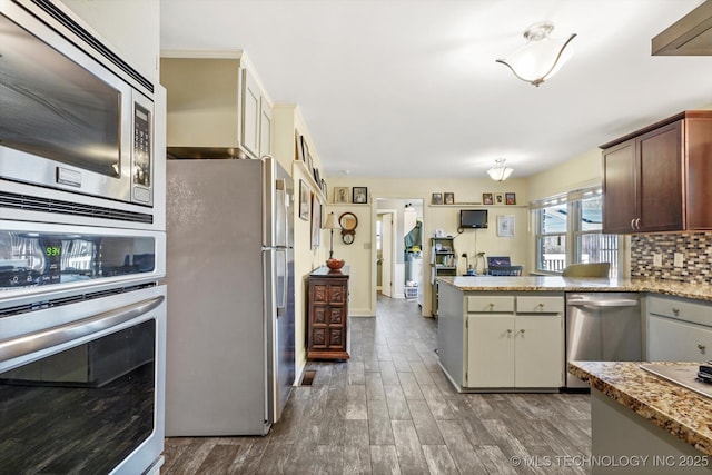 kitchen with backsplash, dark wood finished floors, appliances with stainless steel finishes, a peninsula, and light stone countertops