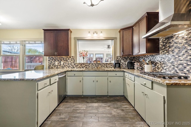 kitchen with a wealth of natural light, decorative backsplash, appliances with stainless steel finishes, wall chimney exhaust hood, and a sink