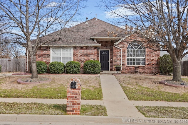 view of front facade with a front yard, fence, brick siding, and roof with shingles