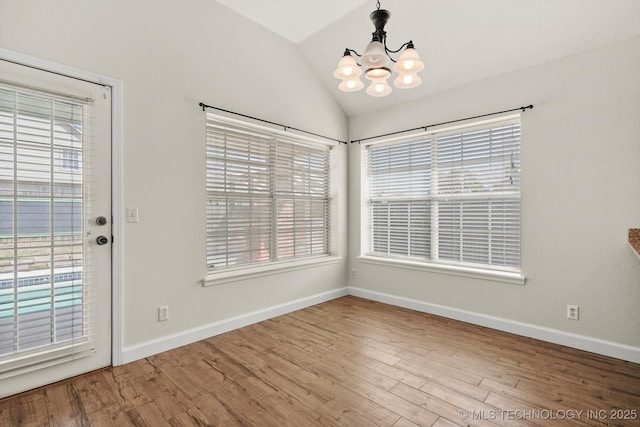 unfurnished dining area featuring baseboards, a notable chandelier, wood finished floors, and vaulted ceiling