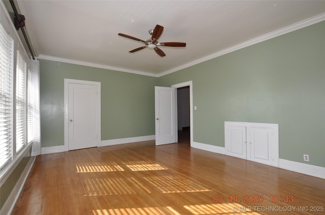 empty room with baseboards, wood finished floors, ceiling fan, and crown molding