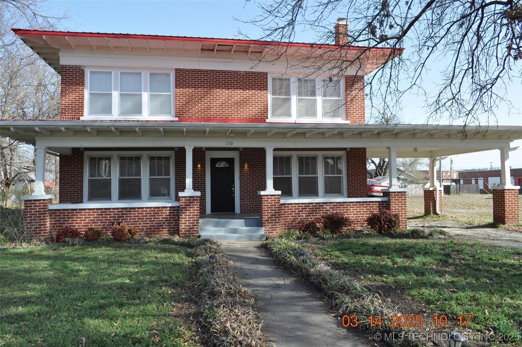 view of front of house featuring a porch, brick siding, a chimney, and a front yard