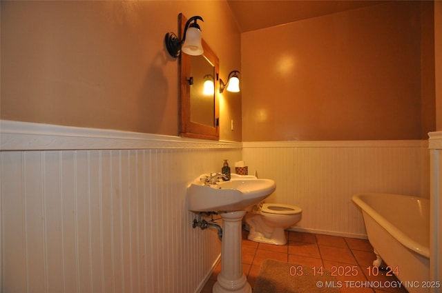 bathroom with tile patterned flooring, a wainscoted wall, toilet, and a freestanding tub