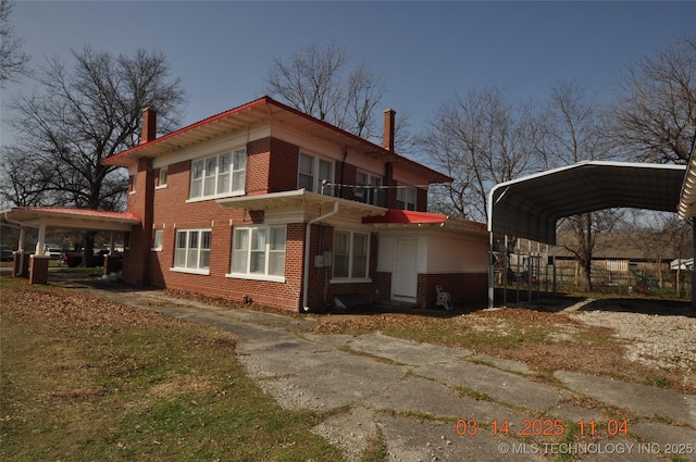 view of home's exterior featuring a balcony, driveway, a chimney, a carport, and brick siding