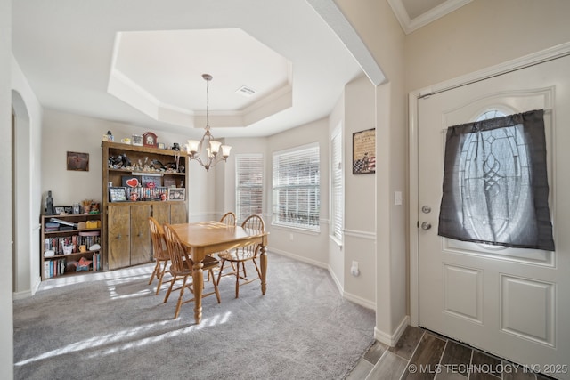 carpeted dining room with visible vents, crown molding, baseboards, a tray ceiling, and a notable chandelier