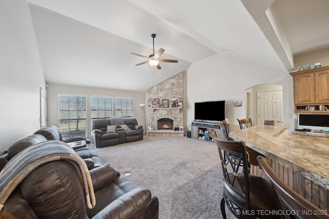 carpeted living area with arched walkways, a stone fireplace, high vaulted ceiling, and a ceiling fan