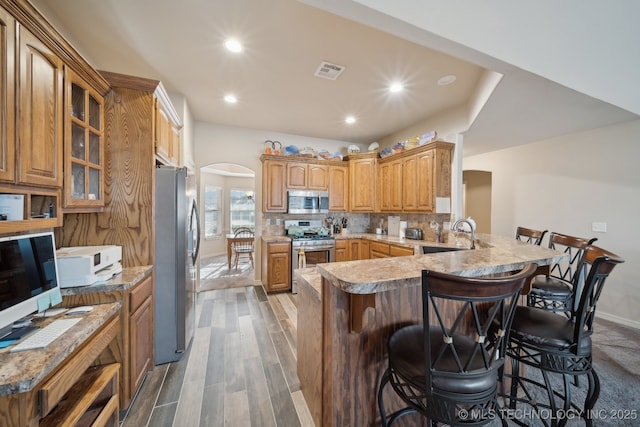 kitchen with visible vents, a peninsula, arched walkways, a sink, and appliances with stainless steel finishes