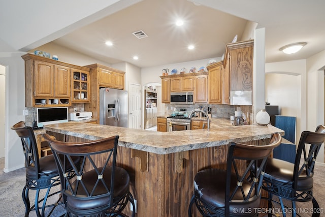 kitchen with glass insert cabinets, light countertops, decorative backsplash, a peninsula, and stainless steel appliances