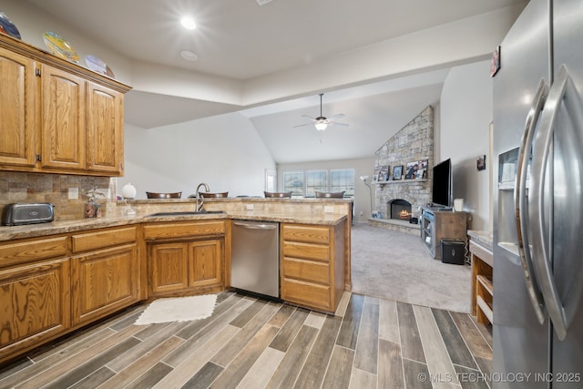 kitchen with a ceiling fan, a sink, appliances with stainless steel finishes, a peninsula, and a fireplace