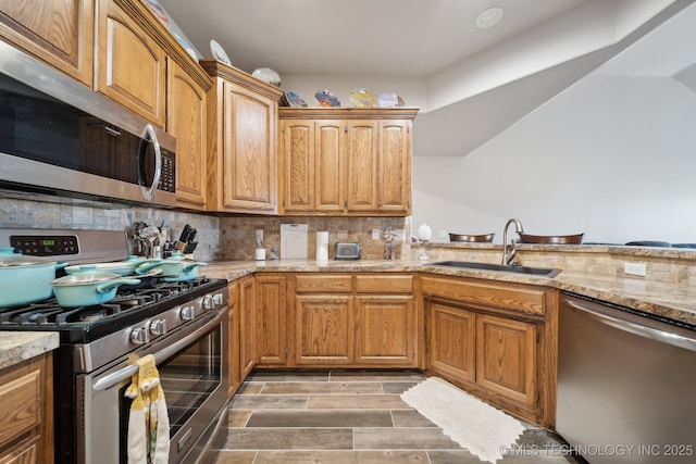 kitchen featuring light stone counters, wood finish floors, a sink, appliances with stainless steel finishes, and backsplash