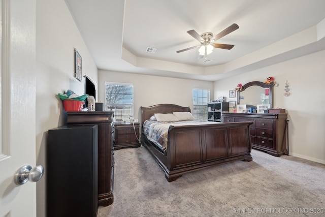 bedroom featuring visible vents, light colored carpet, a raised ceiling, and multiple windows