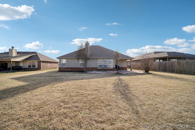 back of house featuring fence, a yard, a chimney, a patio area, and brick siding