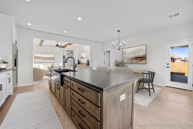 kitchen with visible vents, an island with sink, a sink, dark countertops, and light wood-style floors