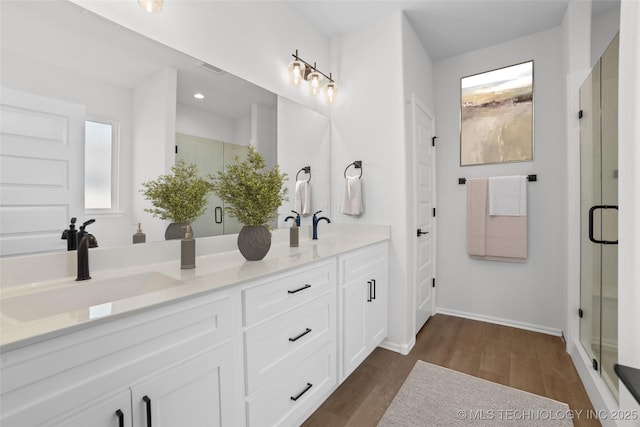 full bathroom with double vanity, a stall shower, wood finished floors, and a sink