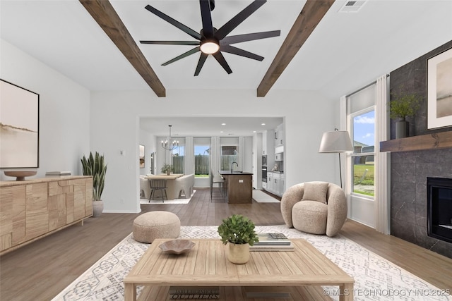 living area featuring visible vents, beamed ceiling, wood finished floors, and a tiled fireplace