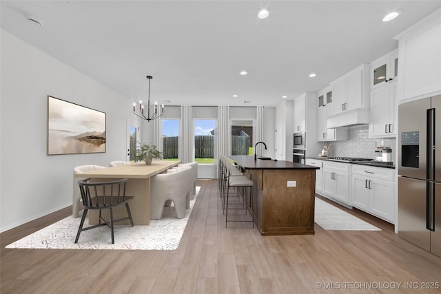 kitchen featuring a breakfast bar, an island with sink, stainless steel appliances, dark countertops, and backsplash