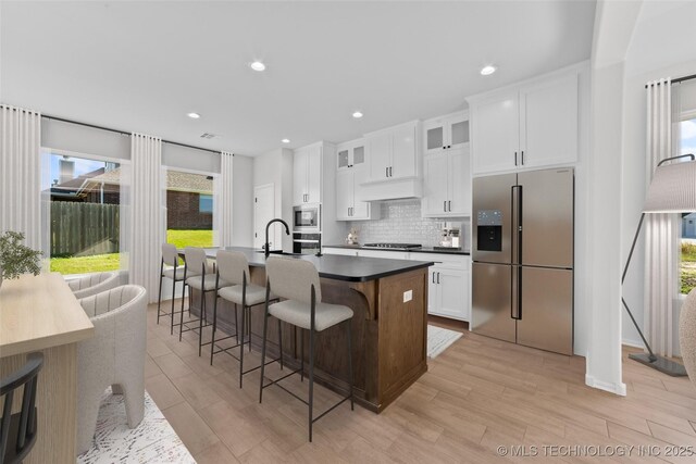 kitchen featuring a breakfast bar area, a center island with sink, appliances with stainless steel finishes, white cabinetry, and backsplash