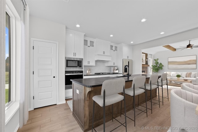 kitchen featuring oven, a center island with sink, decorative backsplash, open floor plan, and built in microwave