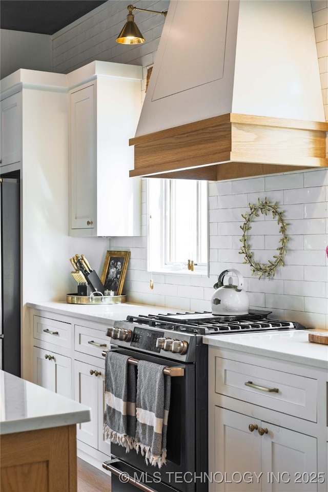 kitchen with white cabinetry, custom exhaust hood, freestanding refrigerator, decorative backsplash, and range with gas cooktop