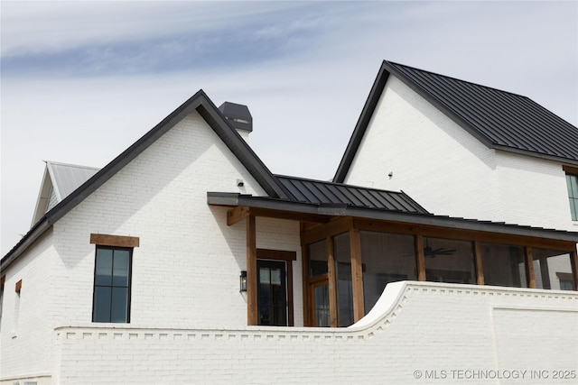 view of side of home featuring metal roof, a sunroom, brick siding, and a standing seam roof