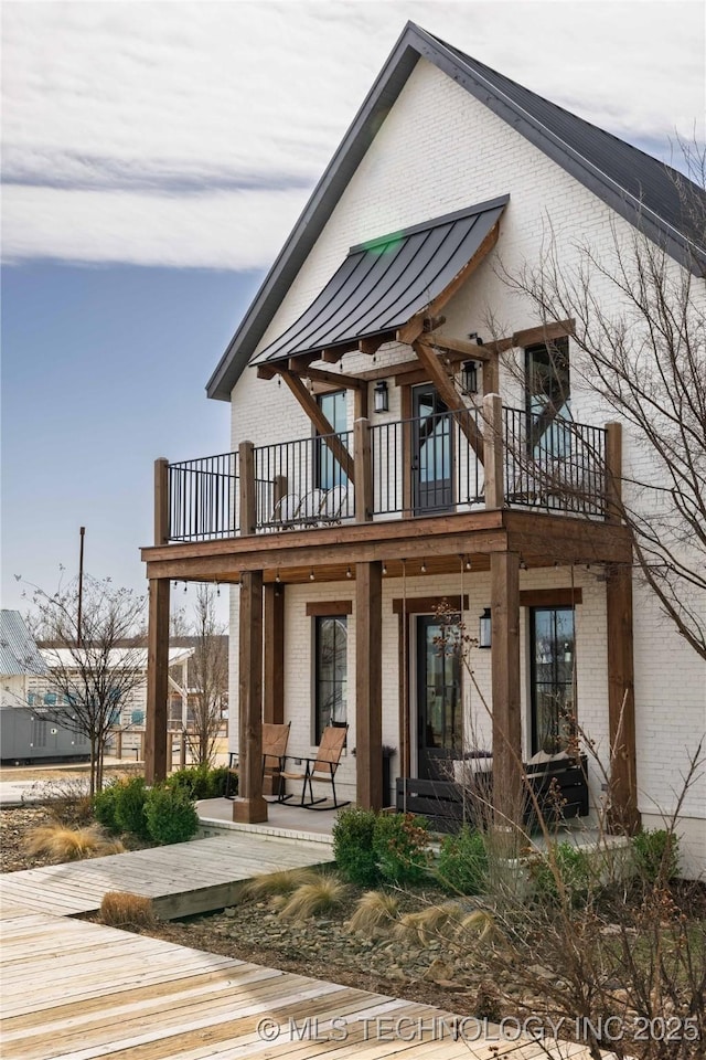 rear view of property with a standing seam roof, a balcony, brick siding, and metal roof