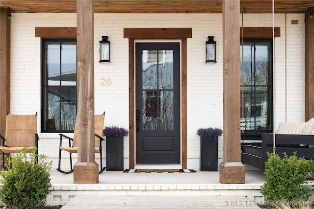 entrance to property with a porch and brick siding