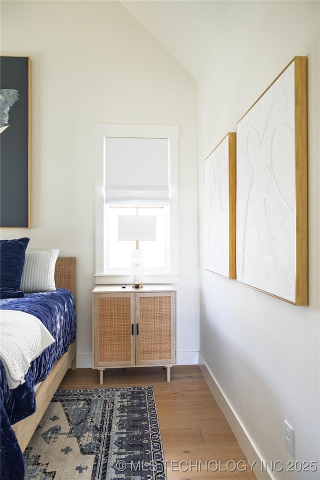 bedroom featuring light wood finished floors, radiator heating unit, baseboards, and vaulted ceiling