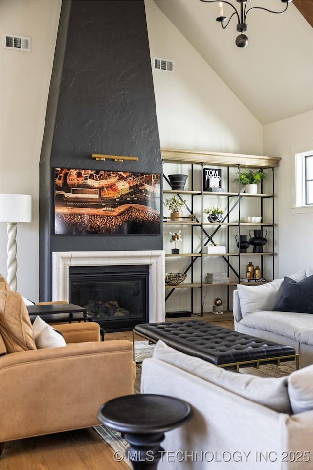 living room with visible vents, wood finished floors, lofted ceiling, and a glass covered fireplace