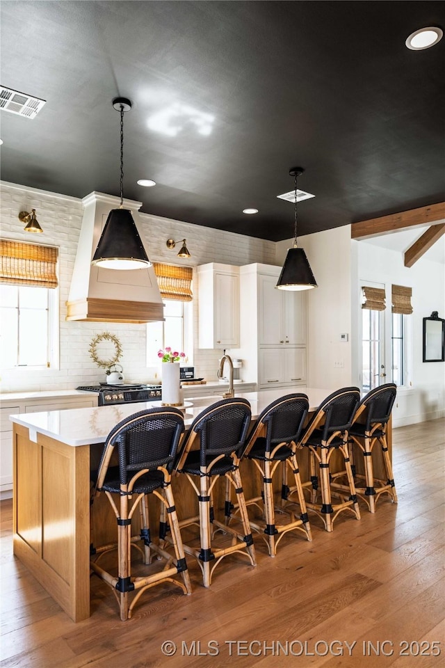 kitchen featuring visible vents, light wood-style flooring, a healthy amount of sunlight, and custom range hood