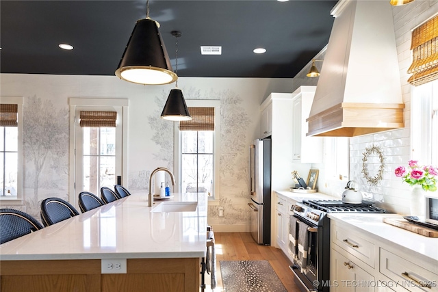 kitchen featuring visible vents, a sink, freestanding refrigerator, range with gas cooktop, and custom exhaust hood