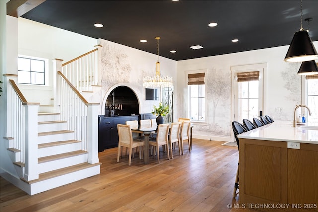 dining area with baseboards, stairs, light wood-type flooring, recessed lighting, and a notable chandelier