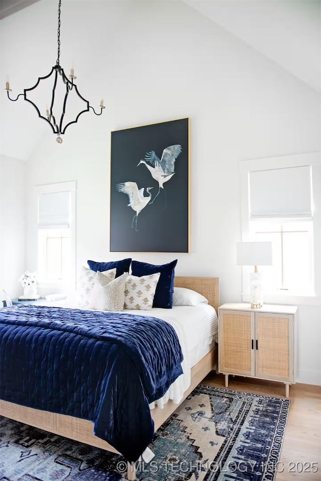 bedroom featuring a notable chandelier, light wood-style flooring, and vaulted ceiling