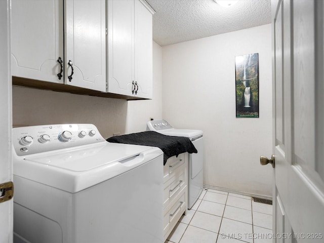 laundry area with a textured ceiling, light tile patterned flooring, cabinet space, and washing machine and clothes dryer