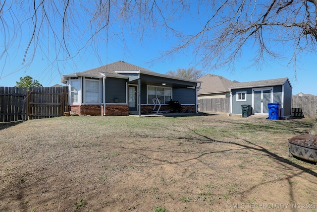 rear view of property with brick siding, a fenced backyard, a lawn, and an outdoor structure