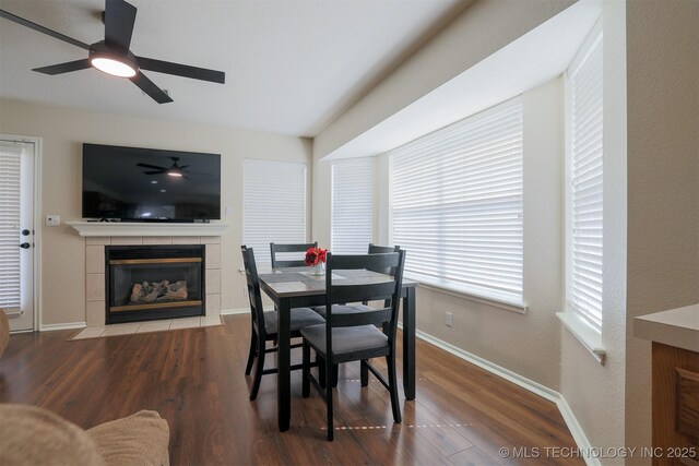 dining room featuring a tiled fireplace, baseboards, a ceiling fan, and wood finished floors