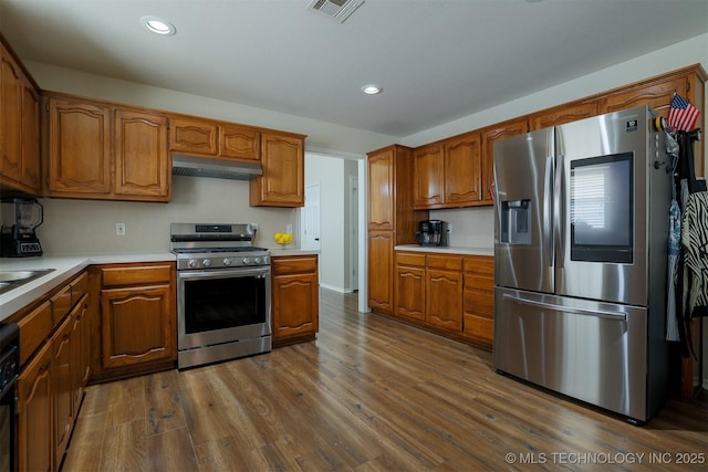 kitchen with under cabinet range hood, brown cabinets, and appliances with stainless steel finishes