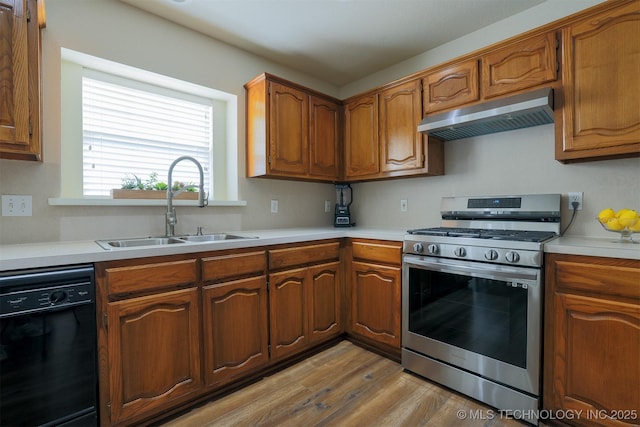 kitchen featuring under cabinet range hood, black dishwasher, light wood-style floors, stainless steel gas stove, and a sink