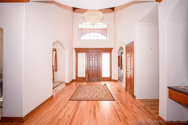 foyer entrance with arched walkways, an inviting chandelier, a high ceiling, and light wood-style floors