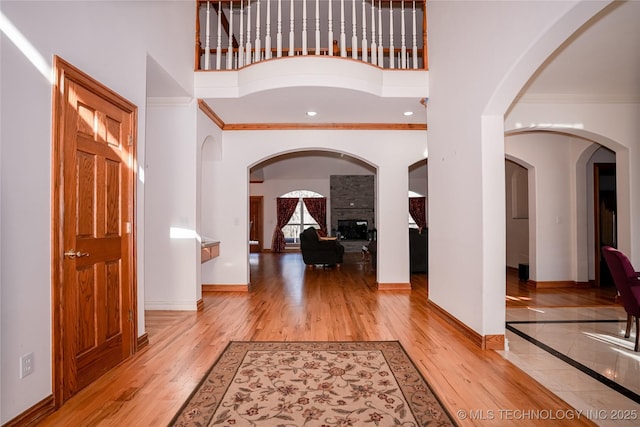 foyer entrance featuring a large fireplace, baseboards, crown molding, a towering ceiling, and wood finished floors