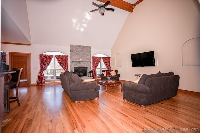 living room with beamed ceiling, light wood-style flooring, a large fireplace, and ceiling fan