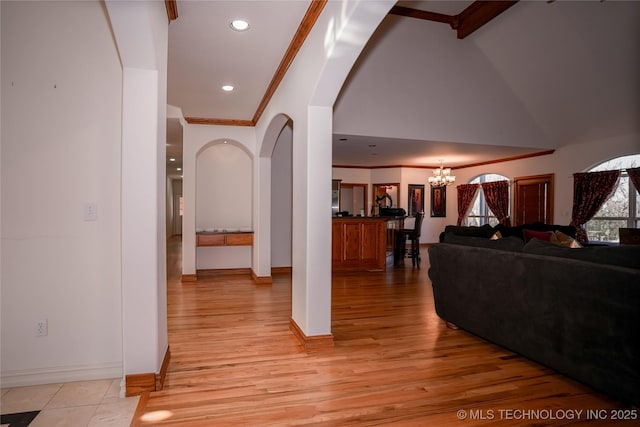 hall with light wood finished floors, lofted ceiling with beams, ornamental molding, an inviting chandelier, and arched walkways