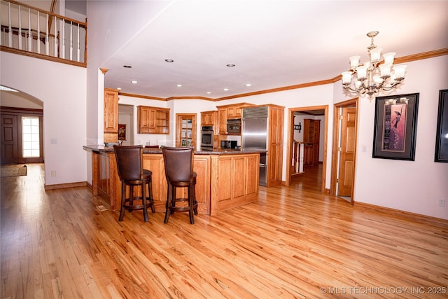 kitchen featuring light wood finished floors, a chandelier, a peninsula, arched walkways, and stainless steel appliances