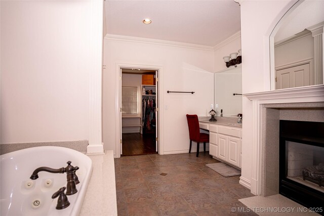 bathroom with vanity, a walk in closet, a whirlpool tub, a glass covered fireplace, and crown molding