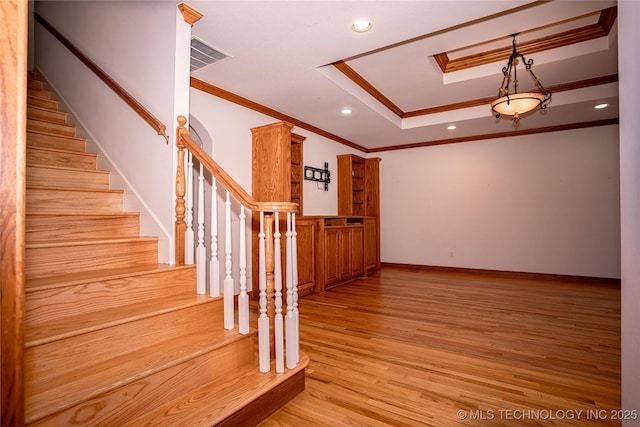 stairway with ornamental molding, a tray ceiling, wood finished floors, recessed lighting, and a skylight